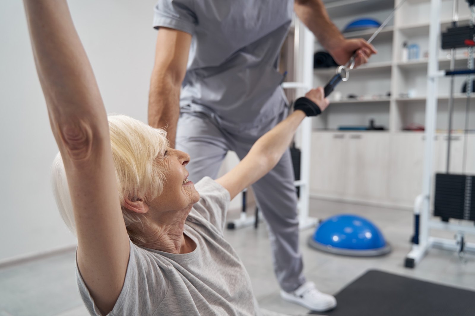 An older woman using exercise equipment with support from her physiotherapist